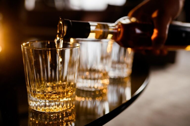 a person is pouring liquor whiskey in glasses